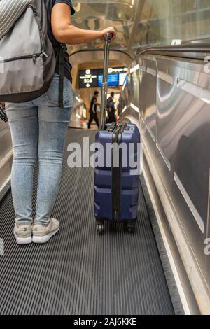 Vertikale Foto der weiblichen Backpacker holding Koffer am Flughafen Rolltreppe Stockfoto
