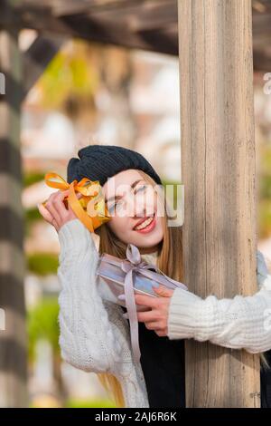 Lächelnd schöne junge Frau hält die Goldenen und Silbernen verpackte Geschenkboxen, während in die Kamera schaut auf eine unscharf Hintergrund. Valentine's anhand von quantitativen Simulatio Stockfoto