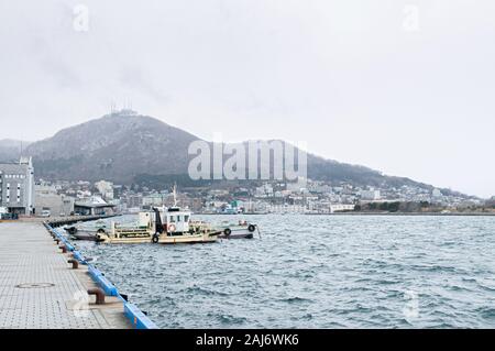 DEC 1, 2018 Hakkodate, Japan -  Hakkodate port Toyokawa pier with fishing boats in winter foggy atmosphere and mount Hakkodate in background. Stockfoto