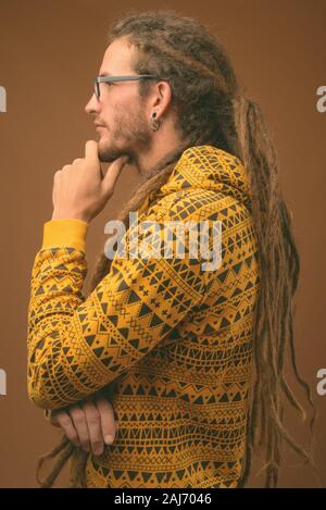 Studio shot von jungen hübschen Hispanic Mann mit Dreadlocks tragen Hoodie gegen braunen Hintergrund Stockfoto