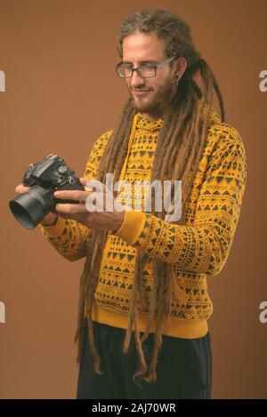 Studio shot von jungen hübschen Hispanic Mann mit Dreadlocks tragen Hoodie gegen braunen Hintergrund Stockfoto
