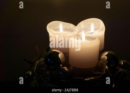 Drei beleuchtete weiße Kerzen und glänzend blau silber Weihnachtskugeln Dekoration auf dunklem Hintergrund Stockfoto