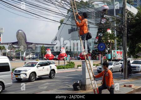 Pattaya, Thailand - Dezember 23, 2019: der Mann, der auf einem Bambus Leiter lehnt sich gegen die power line. Anschlußklemme 21 Shopping Mall auf dem Hintergrund. Stockfoto