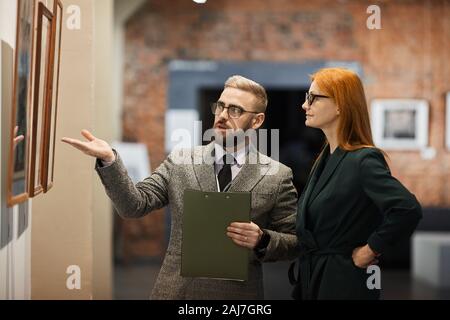 Erfolgreicher Mensch in formale Abnutzung Ordner und zeigen auf Bilder an der Wand er den Ausflug für Frau Stockfoto