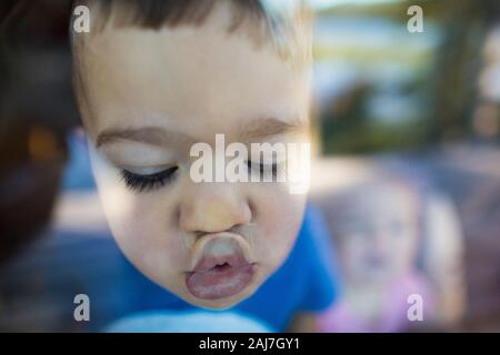 Der junge Junge schiebt seine Lippen gegen ein Fenster, um einen Kuss zu machen Stockfoto