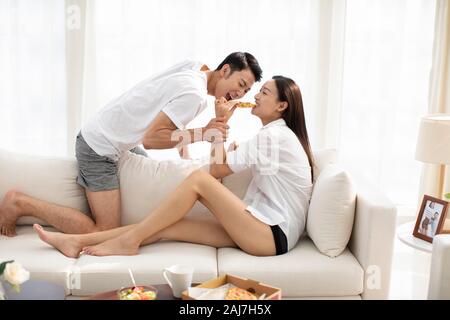Junges chinesisches Paar, das im Wohnzimmer Pizza isst Stockfoto