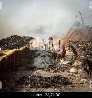 Zwei afrikanische Frauen zwischen dem Fisch sitzen Trocknen auf Hunderte von Holzfachböden in den beißenden Fische trocknen Zone. Fischereihafen in Joal Fadiout, Senegal Stockfoto