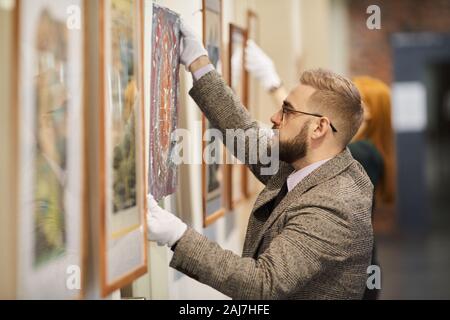 Gut aussehender bärtiger Mann in Brillen und in der Klage hängt das Bild an der Wand und die Vorbereitung für die Kunst Ausstellung zusammen mit Frau Stockfoto