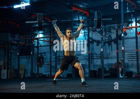 Kaukasischen Menschen üben im Gewichtheben in der Turnhalle. Kaukasier Männlich sportliche Modell Training mit der Langhantel, blickt selbstbewusst und stark. Body Building, gesunden Lebensstil, Bewegung, Aktivität, action concept. Stockfoto