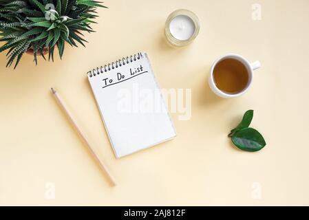 Notebook mit Aufgabenliste, Tasse Kaffee und Pflanzen auf gelb Schreibtisch, Ansicht von oben, kopieren. Planung Konzept. Stockfoto