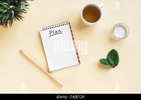 Notebook mit Plan word, Tasse Kaffee und Pflanzen auf gelb Schreibtisch, Ansicht von oben, kopieren. Planung Konzept. Stockfoto