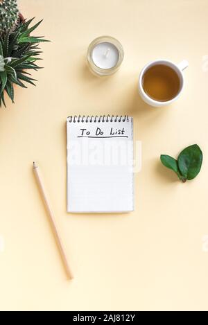 Notebook mit Aufgabenliste, Tasse Kaffee und Pflanzen auf gelb Schreibtisch, Ansicht von oben, kopieren. Planung Konzept. Stockfoto