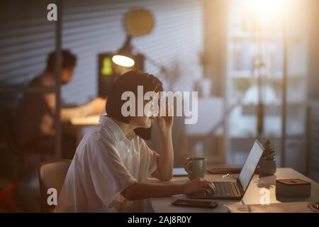Asiatische Geschäftsfrau, Überlastung Arbeiten an dunklen Büro Sie am Tisch sitzen und Arbeiten am Laptop. Stockfoto