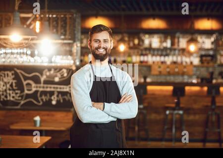 Bärtige lächelnd Barkeeper, Kellner, die auf dem Hintergrund einer Bar. Stockfoto
