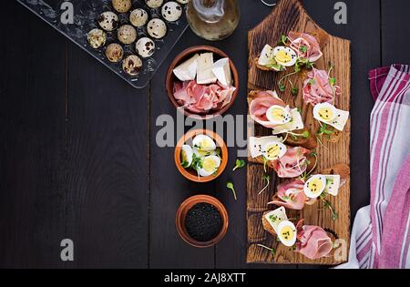 Bruschetta mit Schinken/Jamon traditionelle italienische Antipasti. Leckerer Snack mit Brot, Brie Käse und Wachteln Eier. Gesundheit Lebensmittel, Tapas. Ansicht von oben, Stockfoto