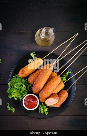 Traditionelle amerikanische Mais Hunde mit Senf und Ketchup auf schwarzem Teller. Street Food. Ansicht von oben, kopieren Raum Stockfoto