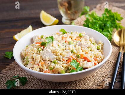 Bulgur mit Huhn, grüne Erbsen und Karotten auf Holz- Hintergrund. Stockfoto