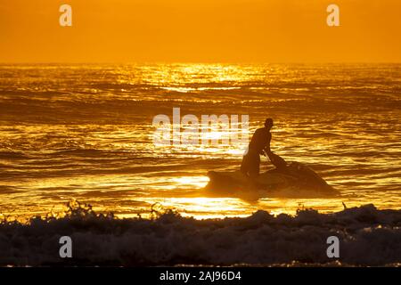 Silhouette der junge Mann, ein Motorrad und den Blick auf den Sonnenaufgang am Horizont der einen schönen Strand Stockfoto
