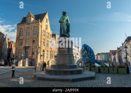 Brügge, Belgien - Oktober 6, 2018: Die Statue von Jan Van Eyck und in den Hintergrund, die Wolkenkratzer von Brügge Studiokca (Wal) aus 5 Tonnen pla Stockfoto