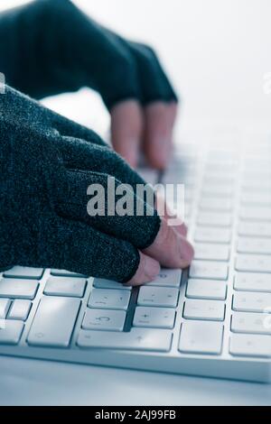 Nahaufnahme von einem kaukasischen Mann tragen ein Paar Handschuhe während der Kompression ist die Eingabe über die Tastatur des Computers Stockfoto