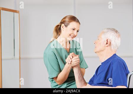 Mann im Rollstuhl Züge seine Hand mit einer Krankenschwester nach einem Schlaganfall Stockfoto