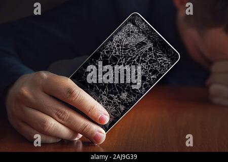 Schön wütend Geschäftsmann, gebrochene Smartphone mit abgestürzt. Einen großen Riss in der Form einer Web auf den Bildschirm des Smartphones. Stockfoto