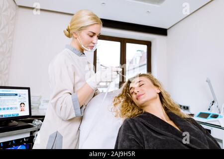 Junge Frau während der professionellen Hydratation Verfahren auf dem Gesicht in den Cosmetological Büro. Professionelle Frau cosmetologyst hält Prustet für Stockfoto