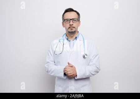 Portrait von ausgewachsenen männlichen Arzt in Brillen und im weißen Mantel mit Kamera vor dem weißen Hintergrund Stockfoto
