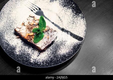 Dessert Schokolade mit Nüssen auf einer großen schwarzen Platte. fein dekoriert Dessert auf dunklen Holztisch Stockfoto