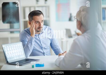 Reifer mann am Tisch sitzen vor dem Arzt und sprechen mit ihm über seine Krankheit bei seinem Besuch im Krankenhaus Stockfoto