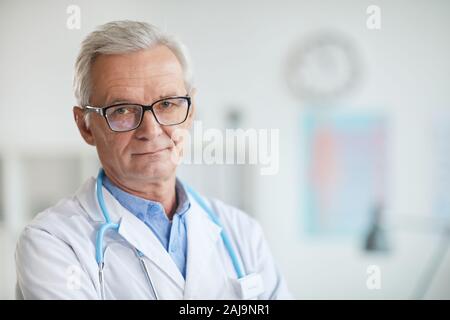 Portrait von erfahrenen Arzt in Brillen und im weißen Mantel, Kamera, während im Büro stehen Stockfoto