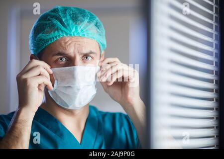 Männliche Chirurgen in der medizinischen Kappe Tragen schützender Maske, während im Büro stehen Stockfoto