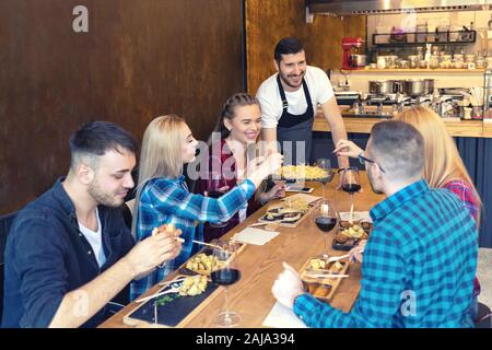 Happy Business Owner essen zu lächeln Gruppe junger Freunde in kleinen familiären Taverne Restaurant. Stockfoto