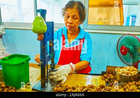 PHUKET, Thailand - 30 april, 2019: Der ältere Arbeitnehmer von Cashew Fabrik verwendet manuelle Schälmaschine für Beschuss von Cashew-nüssen, am 30. April in Phuket Stockfoto