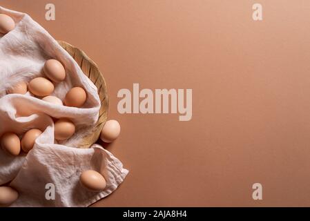 Braune Eier auf Leinen Handtuch und Holzplatte auf braunem Hintergrund. Oben Blick auf Bio Eier. Minimale Ostereier. Huhn Eier frisch gesammelt. Stockfoto