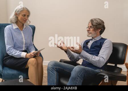 Reifer Psychotherapeut hört ihrem männlichen Patienten zu Stockfoto