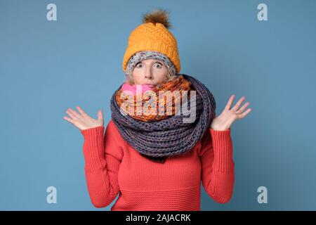 Senior kaukasische Frau in warme Kleidung, Hut, Schal und wirft die Hände zuckte mit den Schultern unsicher, wobei einige Zweifel. Studio shot Stockfoto