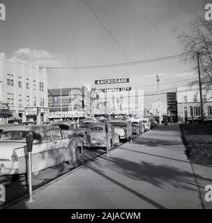 1950er Jahre, historisch, Straßenszene, Anchorage, Alaska, USA, zeigt die amerikanischen Autos der Epoche, die neben der Straße und dem Straßenschild "Anchorage All-America City" geparkt sind. Stockfoto