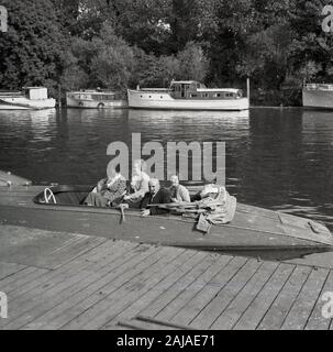 In den 1950er Jahren saßen in einem offenen Motorboot aus Holz der Epoche vier ältere Menschen an einem kleinen Steg neben der Themse in der Nähe von Oxford, England, Großbritannien. Stockfoto