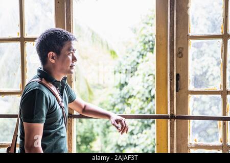 Porträt eines Thailänders, der vor einem offenen Fenster steht Stockfoto