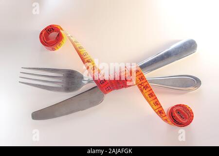 Gewicht zu verlieren. Messer und Gabel sind in einem roten Maßband auf weißem Hintergrund gewickelt Stockfoto