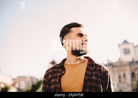 Porträt des selbstbewussten jungen Hipster Mann gegen klaren Himmel in der Stadt Stockfoto