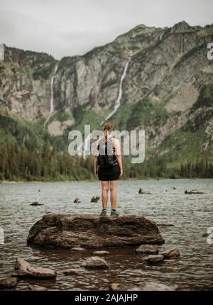 Wandererin mit Rucksack steht auf Felsen in Avalanche Lake, Montana Stockfoto