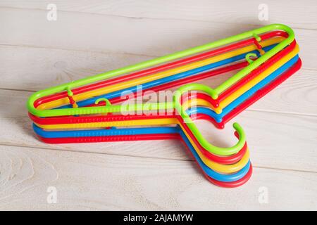 Fünf bunten Kunststoff Kleiderbügel auf hellem Holz- Oberfläche. Satz der neuen bunten Kunststoff Kleiderbügel. Haushaltsgegenstände. Das häusliche Leben. Stockfoto