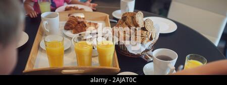 Reichhaltiges Frühstück Tabelle einer Familie auf Urlaub voller Orangensaft, Brot, Croissants, Kaffee und verbreitet. Breite Bild anzeigen. Stockfoto