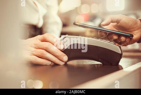 Die Hand des Kunden zahlt sich für das Smartphone im Geschäft mit NFC-Technologie aus. Handy zahlt die Rechnung mit kontaktloser Technologie. Stockfoto