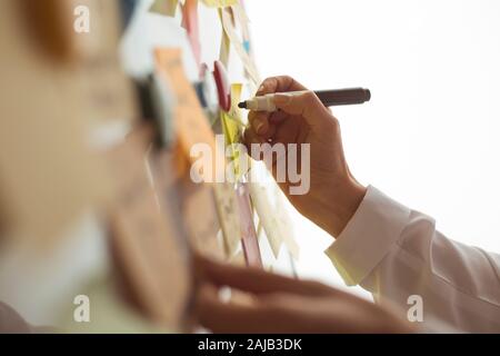 Geschäftsleute schreiben einen wichtigen Hinweis auf, indem sie auf dem Papieraufklebepfosten verwenden. Brainstorming, Teamarbeit. Stockfoto