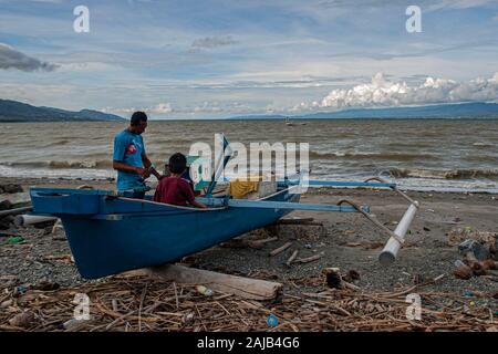 Palu, Indonesien. 03 Jan, 2020. Ein Fischer von seinem Sohn die Reparatur eines defekten Motor begleitet. hohe Wellen in den Gewässern von Palu Bay gezwungen, Hunderte Fischer im Dorf Lere ihre Boote zu verankern. Nach Palu Meteorologie, Klimatologie und Geophysik (BMKG) die Wellen erreicht zwei Meter bis 3 Meter, als ziemlich gefährlich für die Fischer. Credit: SOPA Images Limited/Alamy leben Nachrichten Stockfoto