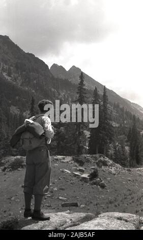 Dreißiger Jahre, historisch, ein männlicher Wanderer, der Plus-Fours und Wanderstiefel trägt und einen Leinwandrucksack trägt, der auf einem Hügel steht und über die Bergketten der Ferne blickt, Jugoslawien. Stockfoto