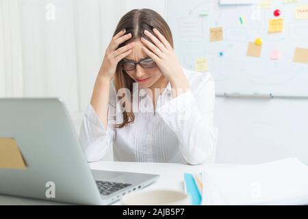 Müde Frau am Computer bei der Arbeit. Kopfschmerzen. Stockfoto